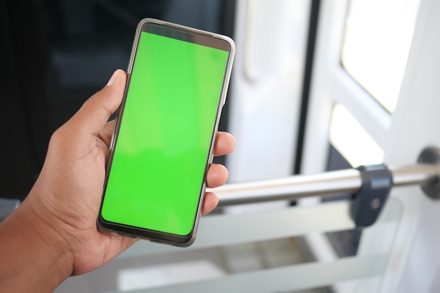 Joven mano usando teléfono inteligente con pantalla verde dentro del tren de metro