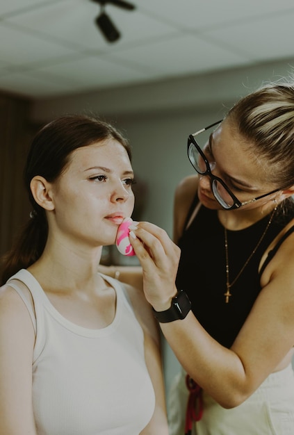 Un joven maquillador aplica la fundación a la cara de una chica