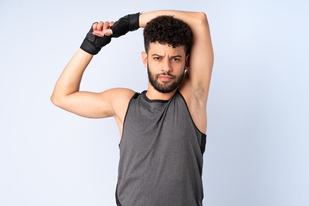 Joven marroquí aislado en la pared azul estirando el brazo