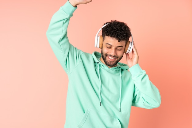 Joven marroquí aislado en la pared rosa escuchando música y bailando