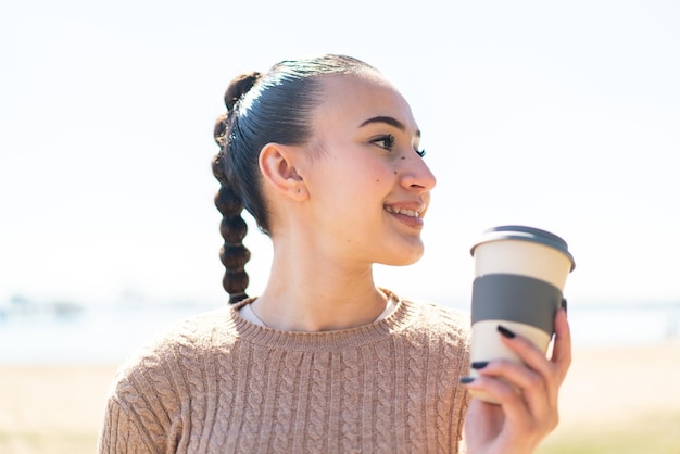 Joven marroquí al aire libre sosteniendo un café para llevar con expresión feliz