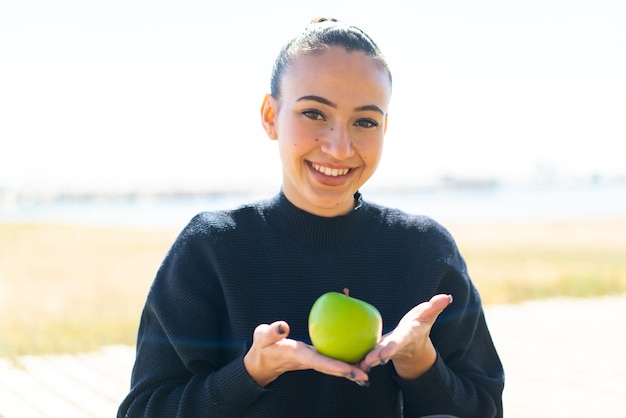 Joven marroquí al aire libre sosteniendo una manzana con expresión feliz