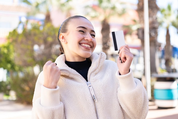 Joven marroquí al aire libre sosteniendo una tarjeta de crédito y celebrando una victoria