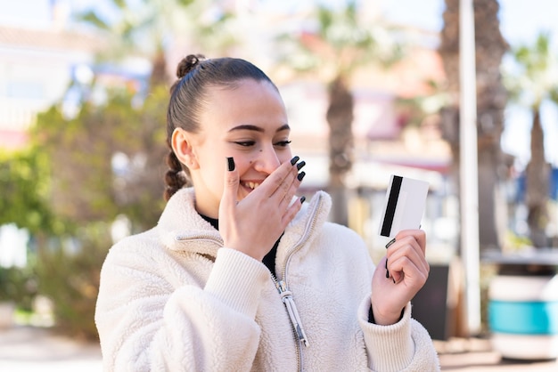 Joven marroquí al aire libre sosteniendo una tarjeta de crédito con expresión sorprendida