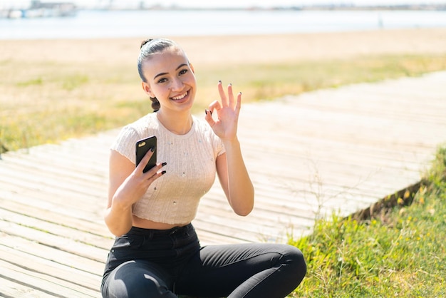 Joven marroquí al aire libre usando teléfono móvil y haciendo el signo de OK