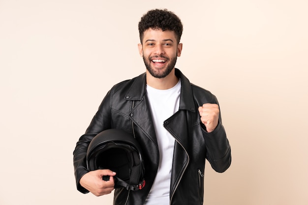 Joven marroquí con un casco de motocicleta aislado sobre fondo beige celebrando una victoria en la posición ganadora