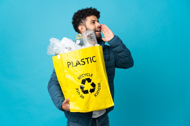 Joven marroquí sosteniendo una bolsa llena de botellas de plástico para reciclar aislado