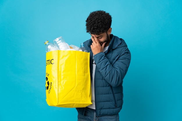 Joven marroquí sosteniendo una bolsa llena de botellas de plástico para reciclar sobre pared aislada riendo