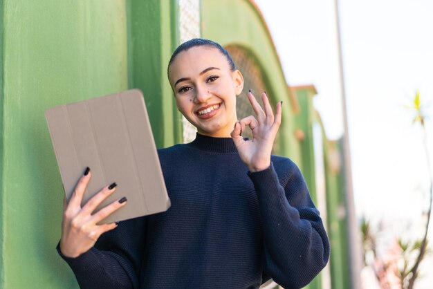 Joven marroquí sosteniendo una tableta al aire libre mostrando el signo de ok con los dedos