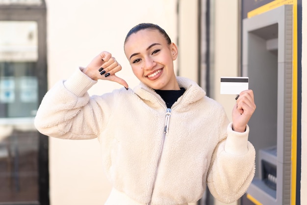 Joven marroquí sosteniendo una tarjeta de crédito al aire libre orgullosa y satisfecha de sí misma