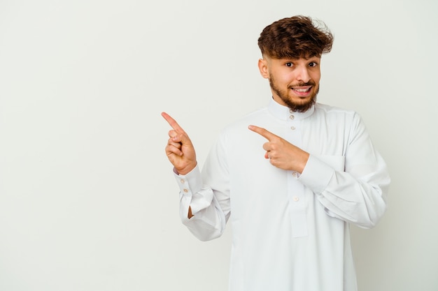 Joven marroquí vistiendo una ropa típica árabe aislado en una pared blanca sorprendido apuntando con el dedo índice a un espacio de copia.