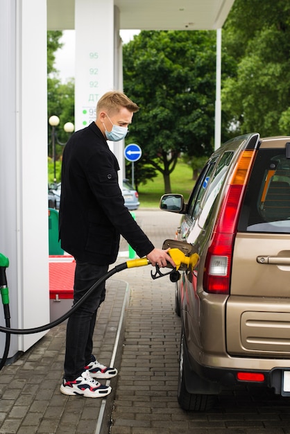 Un joven con una máscara desechable reposta un coche en una gasolinera.