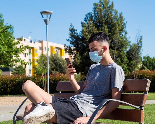 Un joven con una máscara médica en el parque habla por teléfono móvil