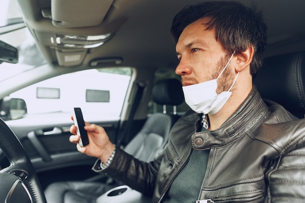 Joven en máscara médica con smartphone en coche