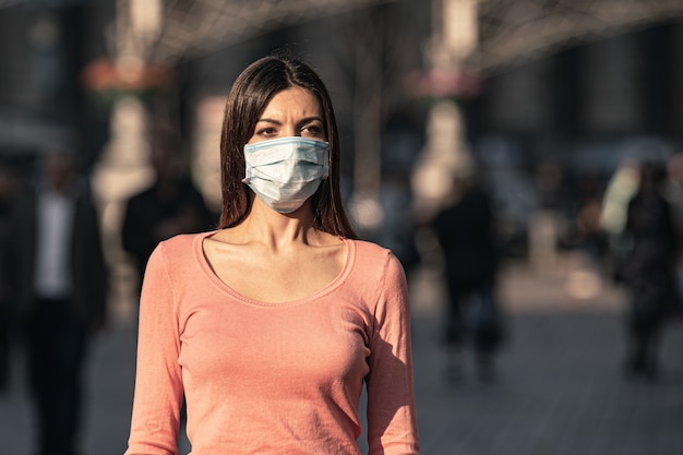 Foto la joven con máscara médica en su rostro se encuentra en la calle urbana