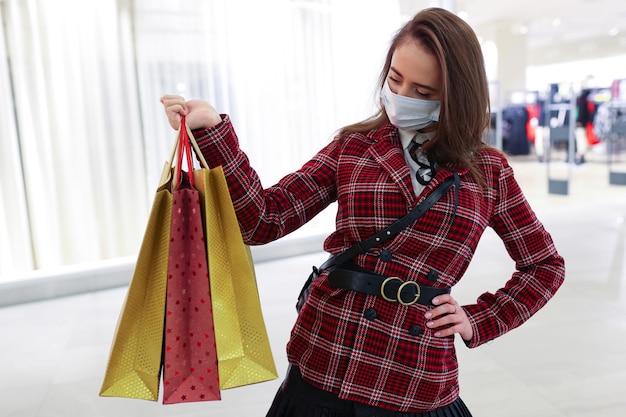 Una joven con una máscara protectora sostiene bolsas de compras en el fondo de un centro comercial