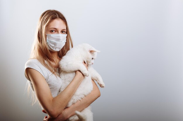 La joven con máscara quirúrgica protectora sostiene a la mascota del gato La enfermedad del coronavirus COVID19 es peligrosa para las mascotas