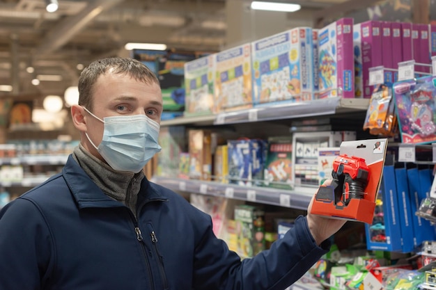 Un joven con una mascarilla protectora elige un juguete en una tienda Día del padre Estilo de vida y seguridad