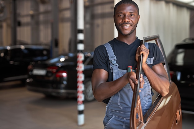 Joven mecánico africano en el trabajo con una parte separada de la máquina