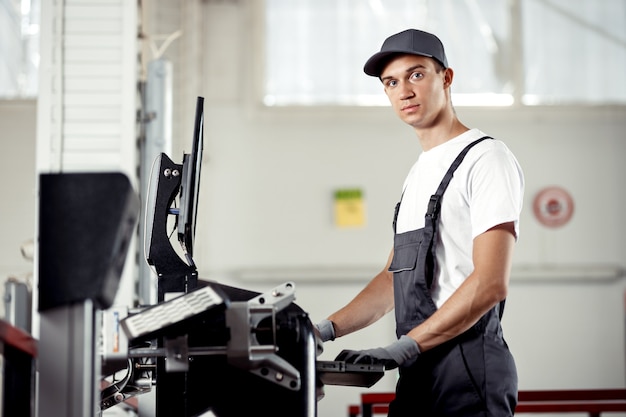 Un joven mecánico de automóviles en uniforme está registrando una computadora que está buscando errores en el motor de un automóvil.