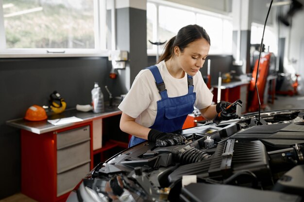 Joven mecánico comerciante trabajando en el motor del automóvil en el garaje de reparación de automóviles