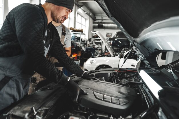 Un joven mecánico examinando el motor bajo el capó del coche en el taller de reparación