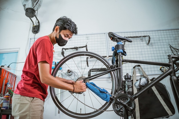 Un joven mecánico en máscara trabajando apretar el eje de la bicicleta