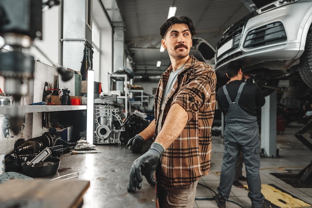 Joven mecánico reparando piezas de automóviles en la mesa de trabajo en el taller de servicio de automóviles