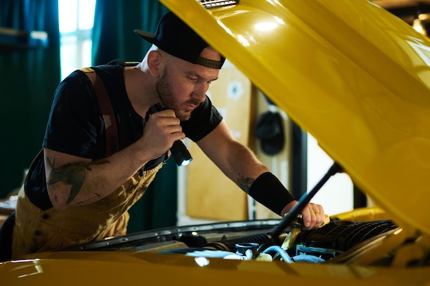 Joven mecánico de taller de reparación de automóviles revisando el motor del automóvil amarillo