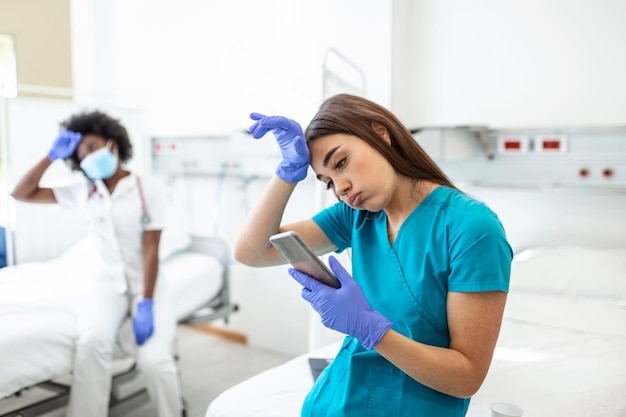 Una joven médica y enfermera tomando un descanso durante la epidemia de covid-19 está usando su teléfono móvil y usando su máscara.