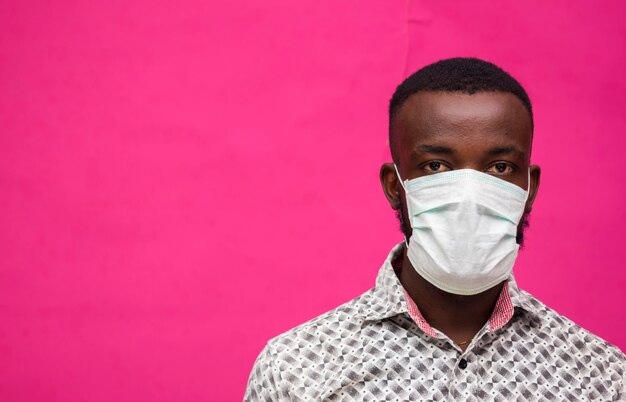 Un joven médico africano aislado sobre fondo rosa con mascarilla para evitar el brote, la enfermedad y la gripe.