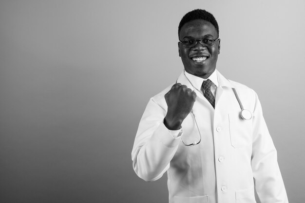 Joven médico africano con anteojos contra la pared blanca. en blanco y negro