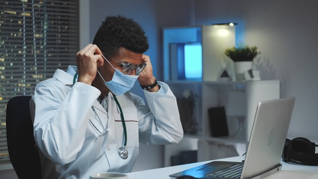 Joven médico africano que muestra cómo usar una máscara médica por video llamada en la computadora