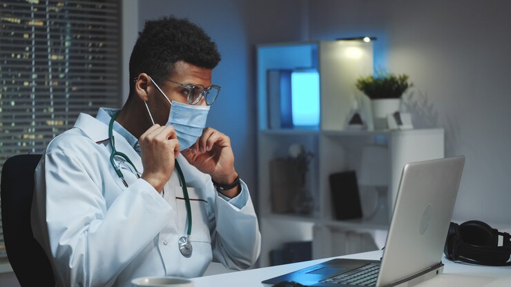 Joven médico africano que muestra cómo usar una máscara médica por video llamada en la computadora