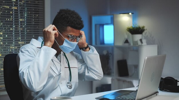 Joven médico africano que muestra cómo usar una máscara médica por videollamada en la computadora