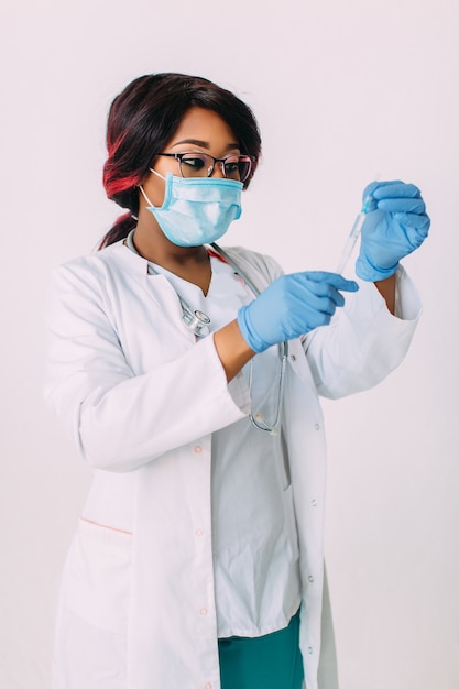 Joven médico afroamericano sonriente en máscara médica sosteniendo una jeringa