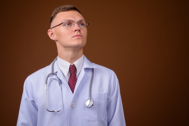 Joven médico con anteojos contra el fondo marrón