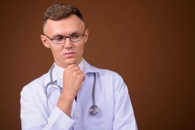 Joven médico con anteojos contra el fondo marrón