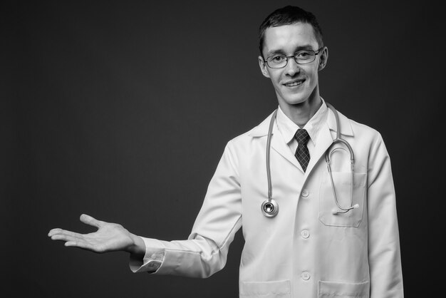 Joven médico con anteojos contra la pared gris en blanco y negro