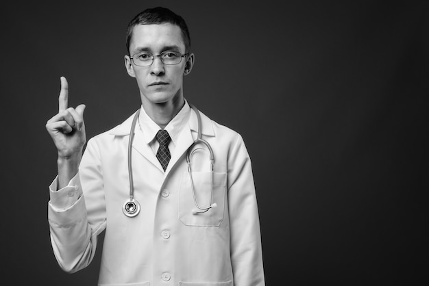 Joven médico con anteojos contra la pared gris en blanco y negro