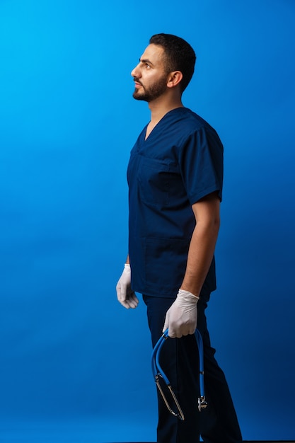 Joven médico árabe de pie contra el fondo azul.