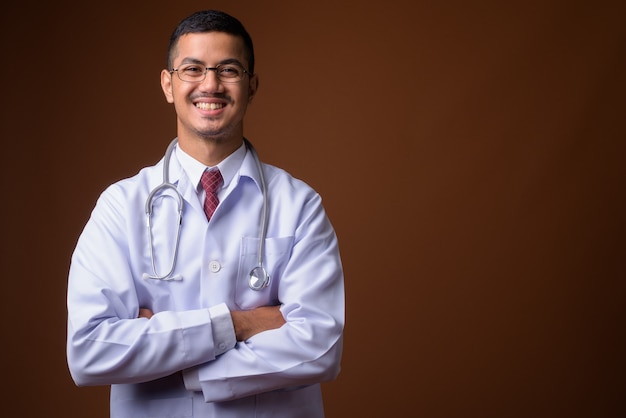 Joven médico asiático multiétnico contra la pared marrón