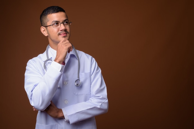 Joven médico asiático multiétnico contra la pared marrón