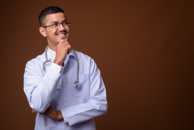 Joven médico asiático multiétnico contra la pared marrón