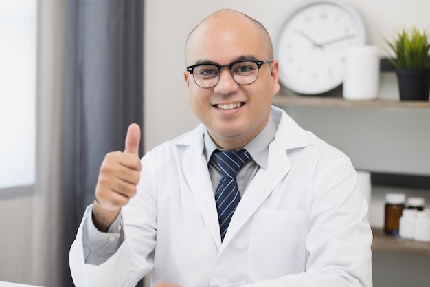 Un joven médico asiático trabaja desde casa trabajando en línea mirando y hablando en cámara con el paciente. Explicar acerca de tomar medicamentos para tratar enfermedades.