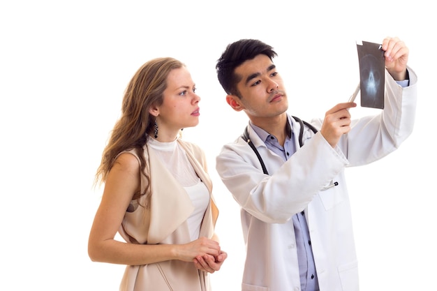 Joven médico de aspecto inteligente con vestido blanco con estetoscopio que muestra rayos X a una mujer joven y hermosa