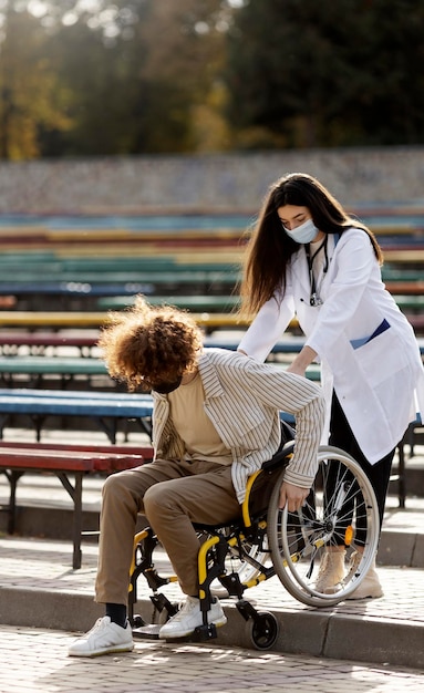 Un joven médico ayuda a un paciente a bajar las escaleras Un médico con una máscara protectora se preocupa por un paciente discapacitado