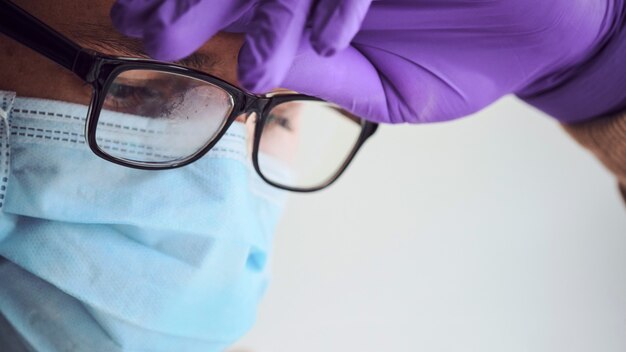 Joven médico cansado en máscara médica, gafas empañadas y guantes desechables.