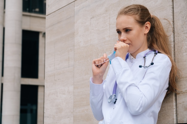 Joven médico caucásico en una máscara protectora tose en la calle