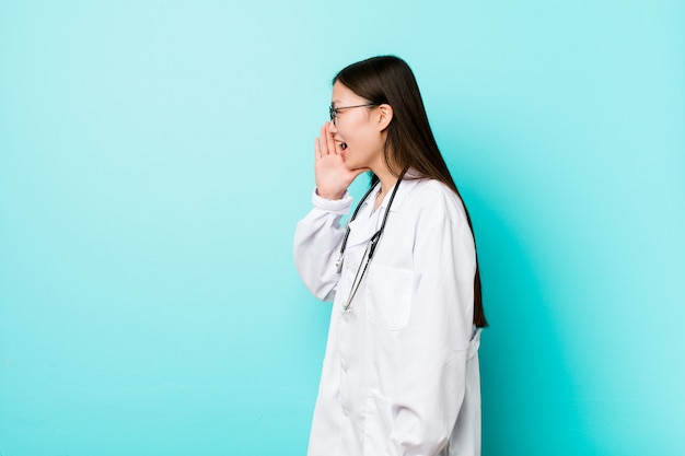 Foto joven médico chino mujer gritando y sosteniendo la palma cerca de la boca abierta.